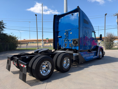 Kenworth T680 conventional sleeper tractor rear view showing dual rear axles, chrome wheels, blue paint, and fifth-wheel coupling.