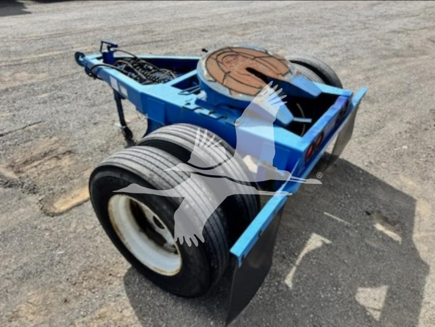 Dolly trailer component showing blue chassis and large dual tires, with a circular reel toward the rear, wheel fenders, and visible steel framework.