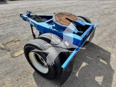 Dolly trailer component showing blue chassis and large dual tires, with a circular reel toward the rear, wheel fenders, and visible steel framework.
