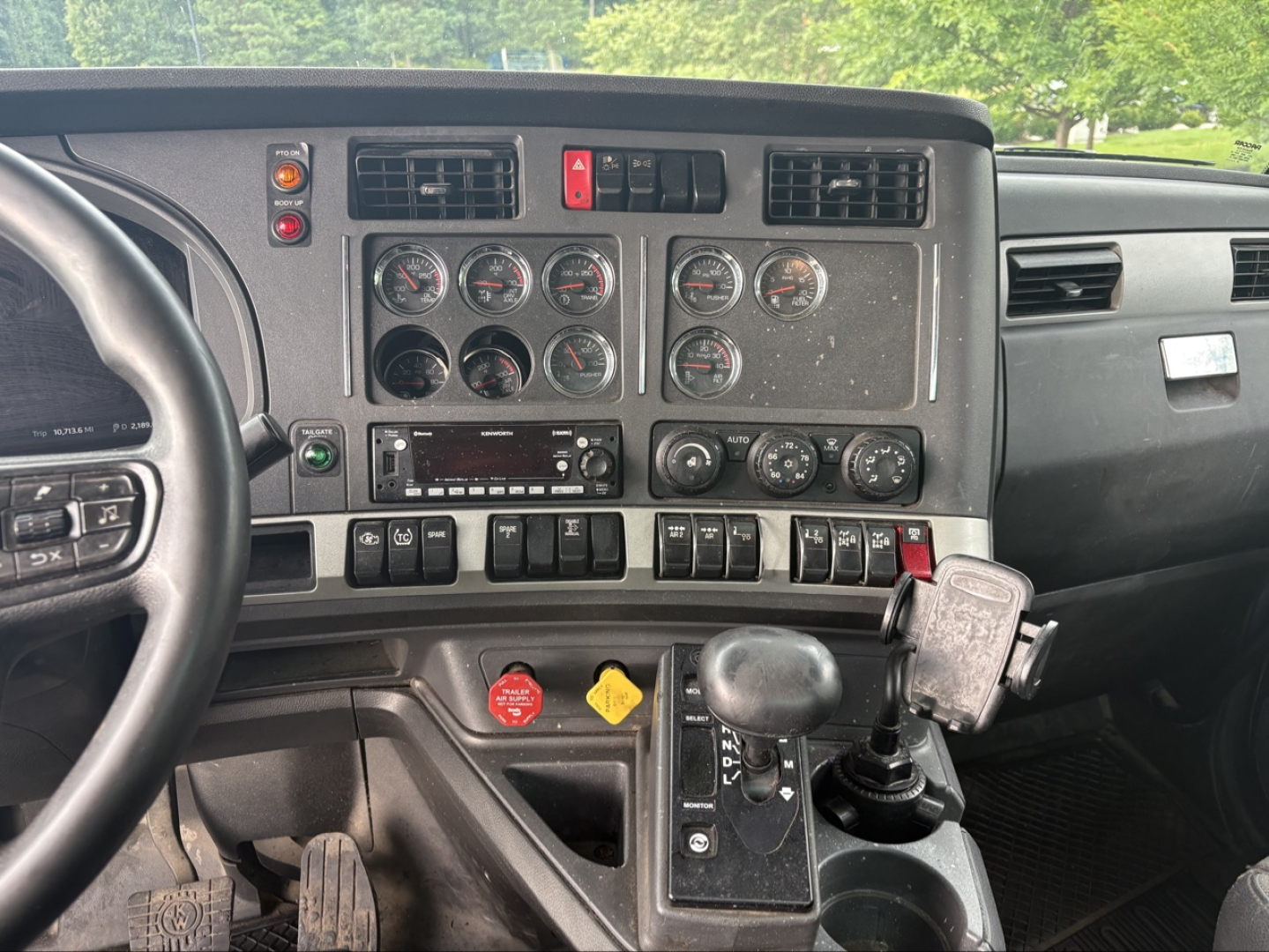 Kenworth T880 cab interior dashboard showing gauges, controls, gear selector, and steering wheel with attached device mount.
