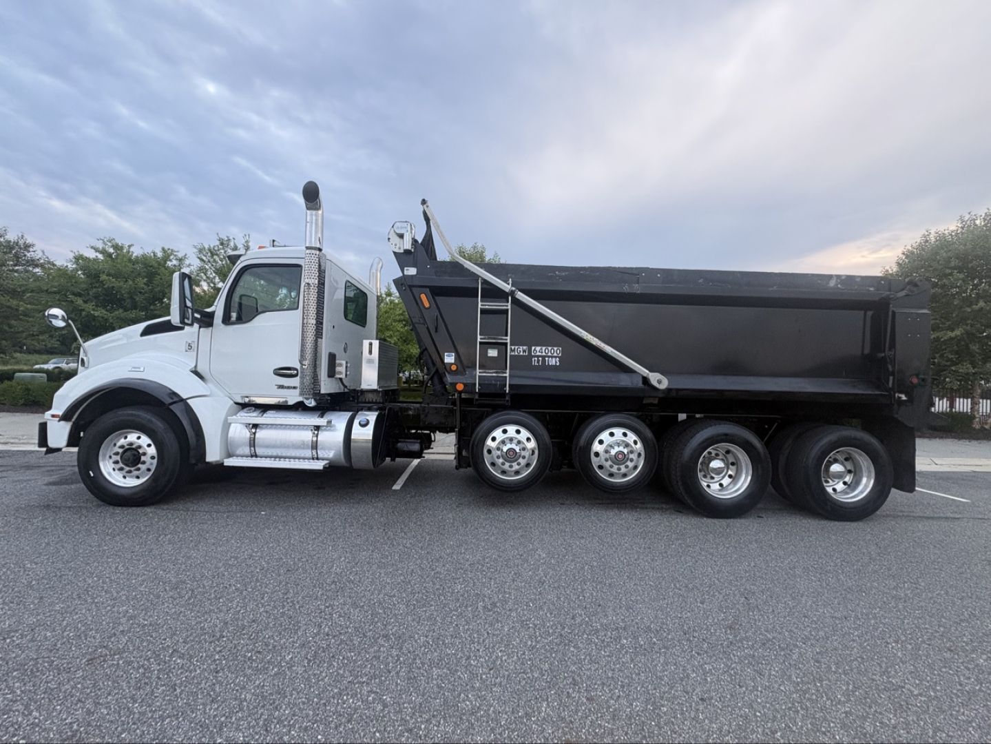 Kenworth T880 dump truck side view showing black dump body and white cab with chrome exhaust stacks.