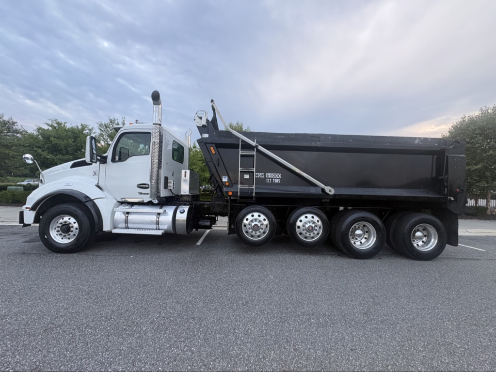 Kenworth T880 dump truck side view showing black dump body and white cab with chrome exhaust stacks.