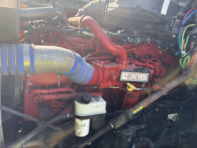 Kenworth T880 engine bay showing 4X15 badge on red engine, blue braided hose, white coolant reservoir, wiring harnesses, and surrounding components.