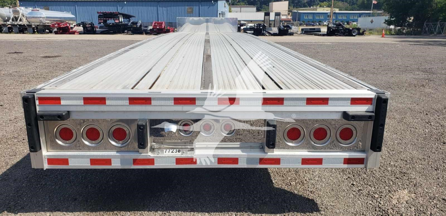 Trailer rear view showing aluminum dropdeck with multiple circular taillights and reflective red-white tape.
