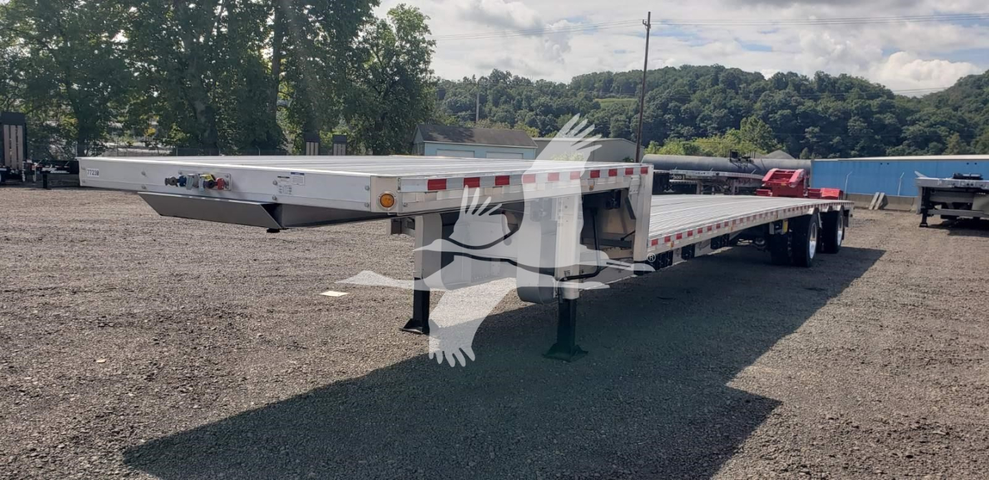 Flatbed trailer showing dropdeck low-profile design with tandem axles and support legs, from a rear three-quarter view.
