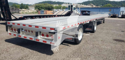 Dropdeck trailer showing steel chassis with dual rear axles and reflective safety markings.