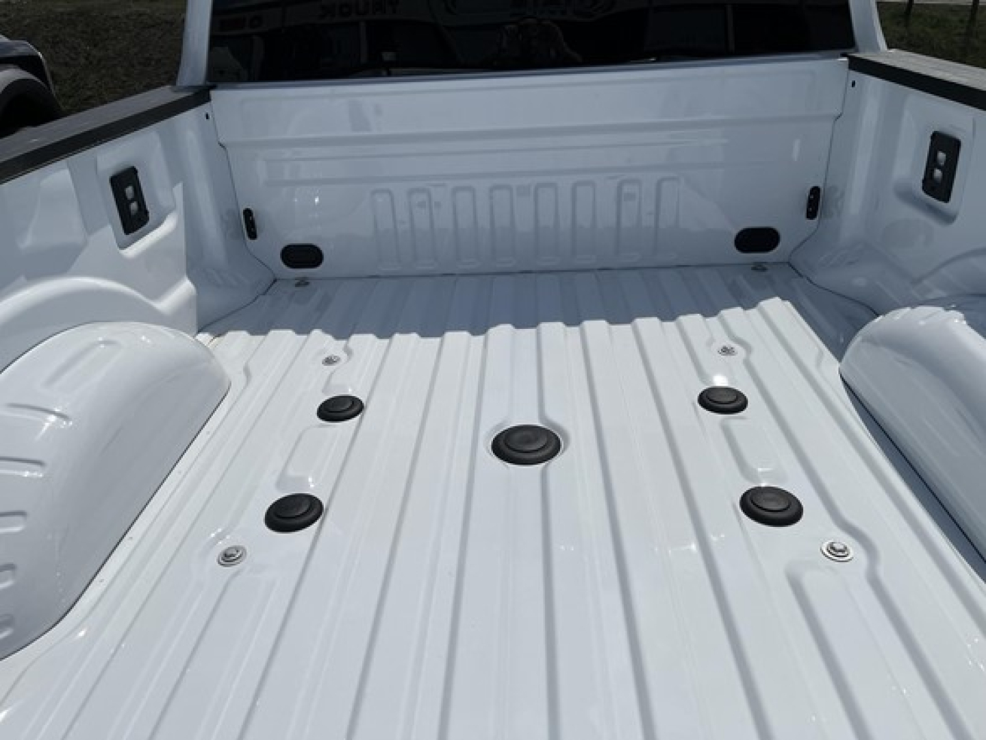 Truck bed of a white 2026 Ford F350 with cargo tie-down anchors and wheel wells visible.