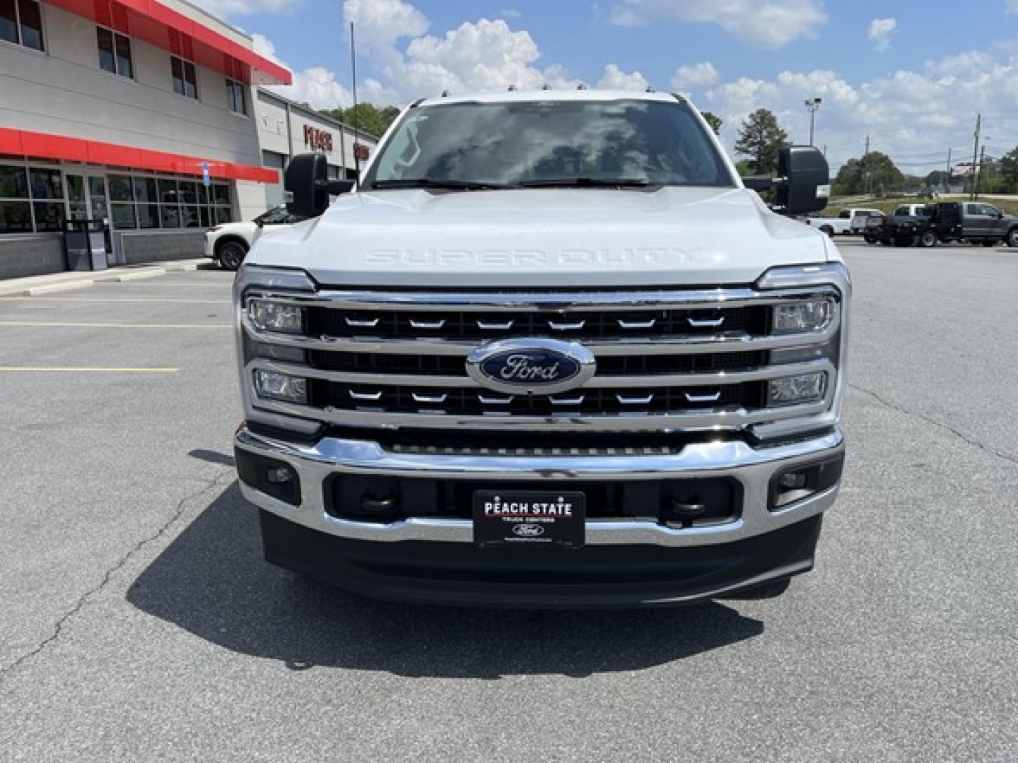 Front view of a white 2026 Ford F-350 pickup truck with chrome grille and Ford emblem, showing large bumper and headlights in a dealership lot.