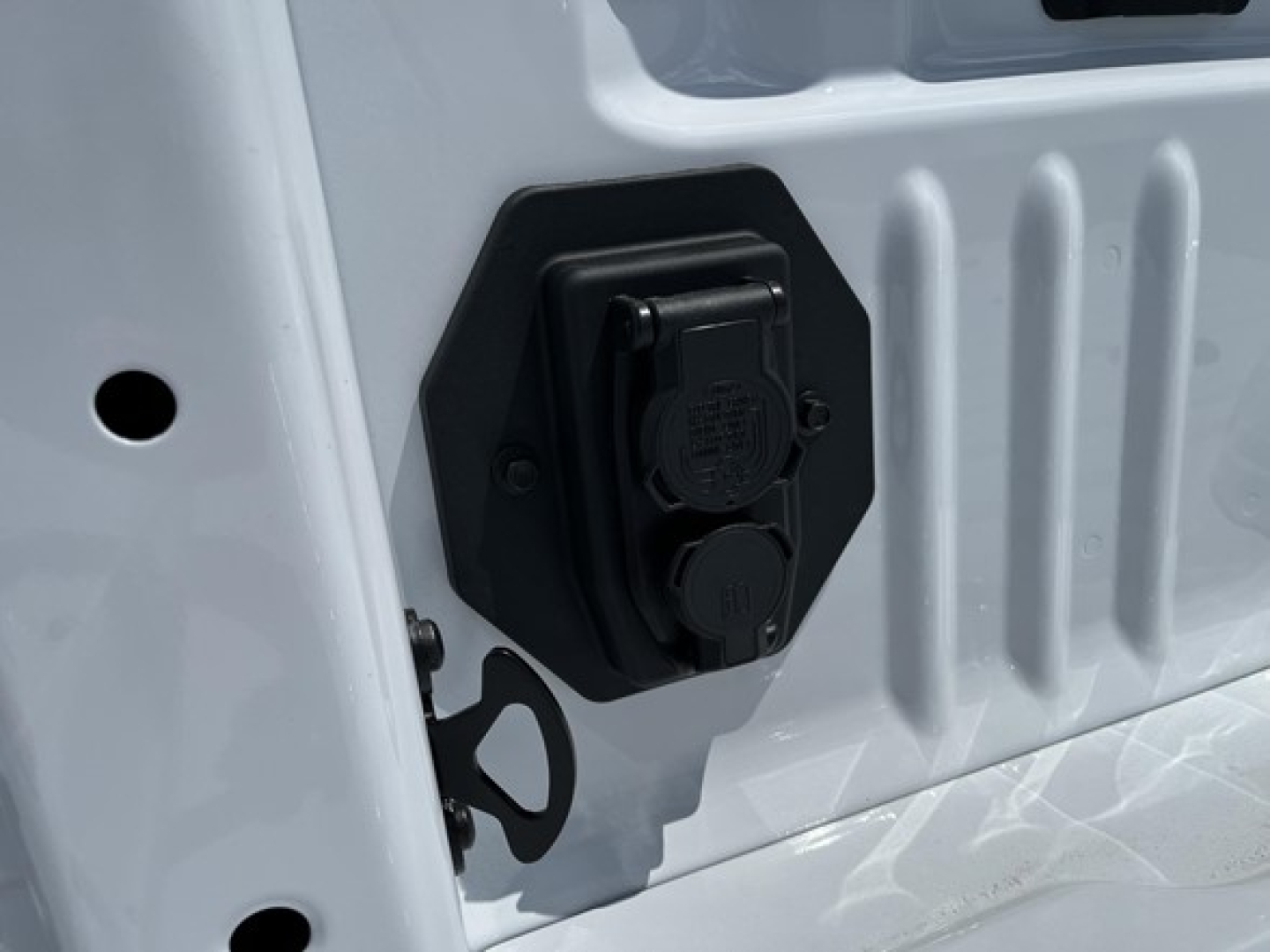 Truck power outlet/fuse panel on white Ford F-350 bed wall with two black circular outlets and surrounding hex mounting plate.