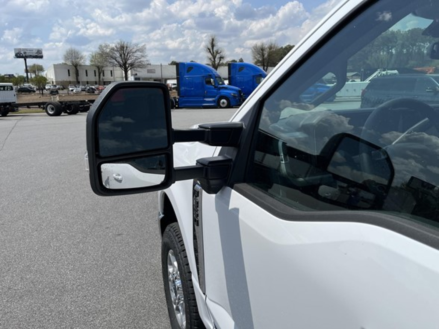 Ford F-350 pickup truck side mirror and front door area in white paint with blue trailers in background.