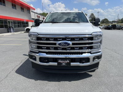Front view of a white 2026 Ford F-350 pickup truck with chrome grille and Ford emblem, showing large bumper and headlights in a dealership lot.