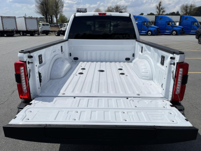 Truck bed of a 2026 Ford F350 with open tailgate and white cargo bed showing wheel wells and tie-downs.