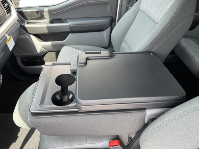 Truck interior: center console with integrated cupholders and storage, fold-down armrest between front seats; light gray fabric seats; part of dashboard visible.