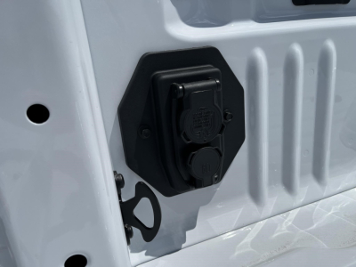 Vehicle image showing a close-up of a dual 120V/240V power outlet on the side of a white Ford F-350 bed with protective black housing.