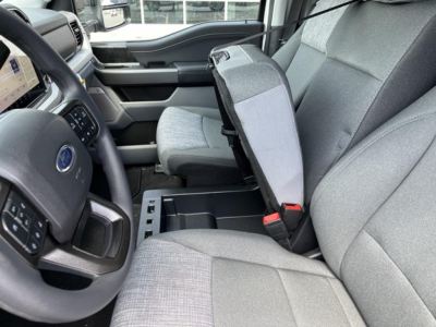 Ford F-350 interior showing front seats, center console, and open fold-down seat in gray fabric; steering wheel and dashboard visible on left.