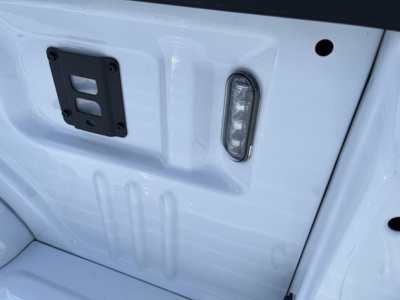 Ford F-Series 2026 SUV? tailgate area showing rear step light and hitch mount bracket, white paint, VIN plate area not visible.