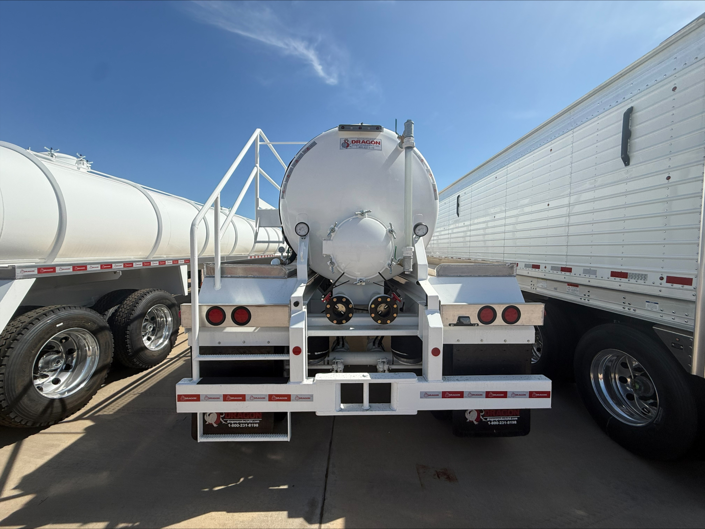 Trailer rear view showing a cylindrical tank with a round manhole and dual rear work lights, on a white aluminum frame with reflective strips.