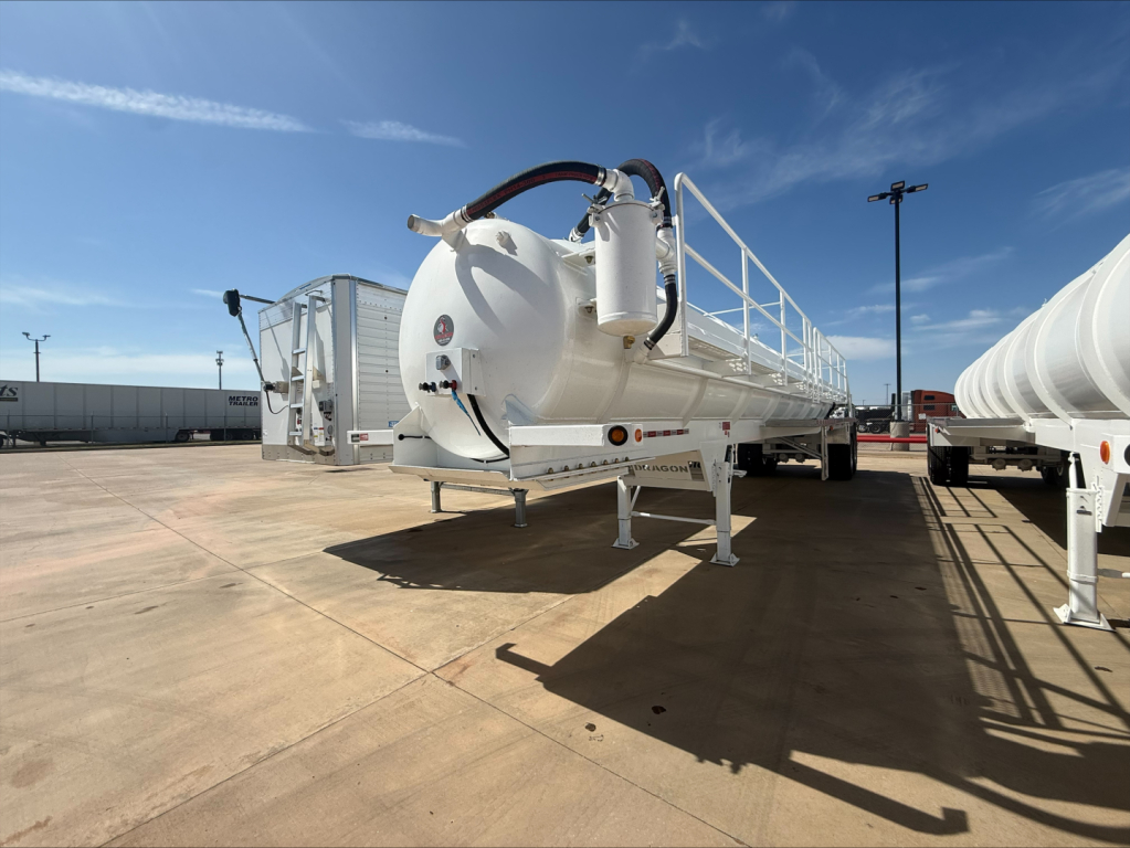 Tank trailer in a lot showing front view with large round white cylindrical tank, hoses and a pump, on a dual-axle trailer.