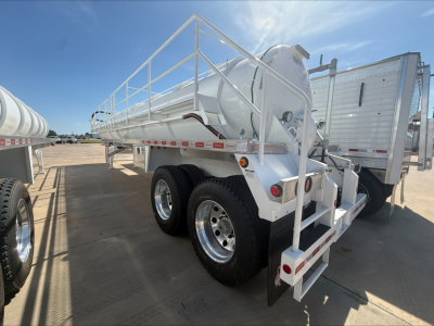 Trailer showing cylindrical tank with railings on top, tandem axle wheels, rear stairs and mud flaps. Labels and safety rails visible along frame.