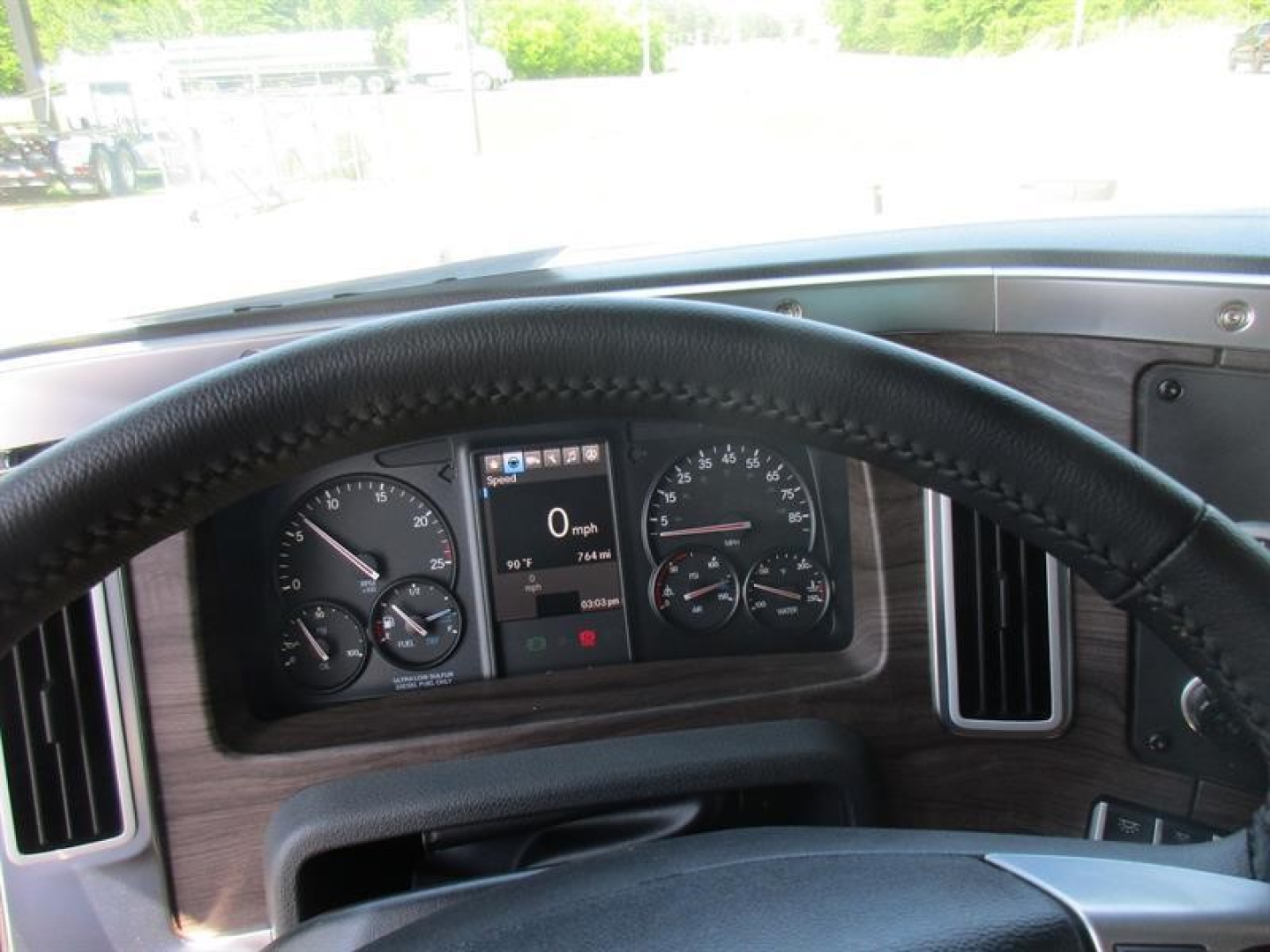 Truck cockpit view showing steering wheel and instrument cluster in a Western Star 49X; dash with gauges and a central digital display reading 0 mph.