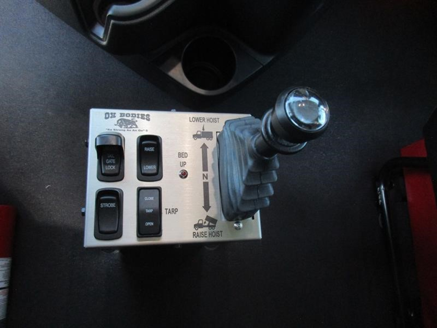 Industrial truck control panel and joystick in-drive gear selector area with labeled switches and diagram reading ‘lower hoist’ and ‘bed up’ on metal plate.