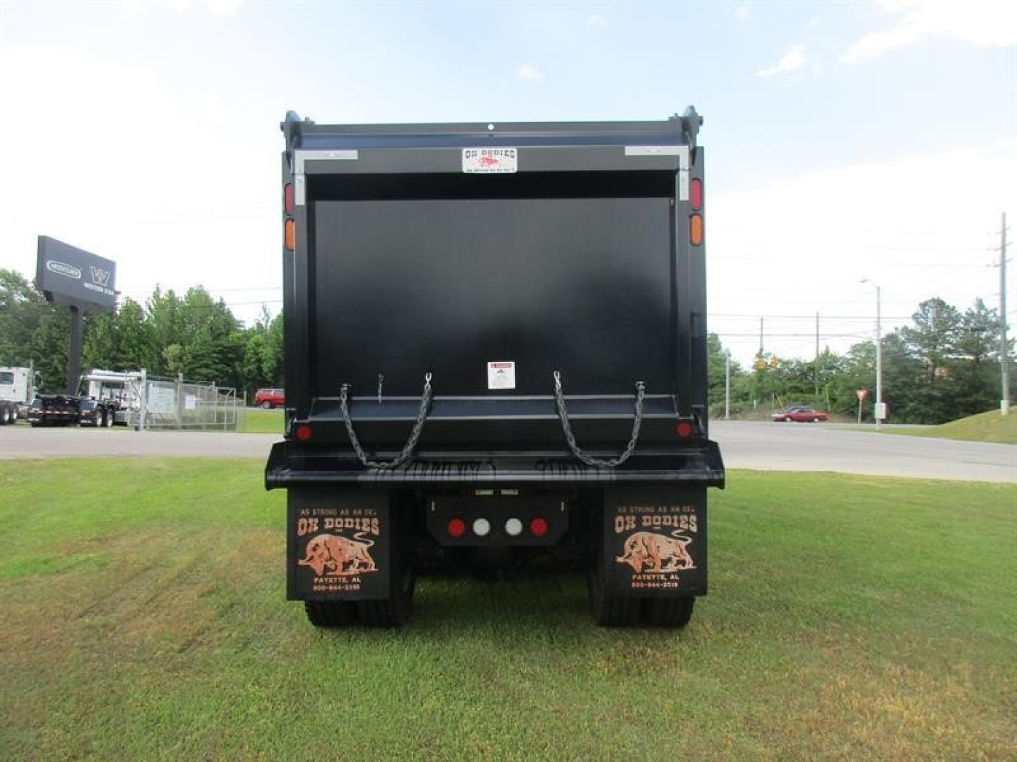 Dump truck rear showing mud flaps with graphic, rear bumper with lights, and open cargo bed of a new Western Star 49X dump truck.