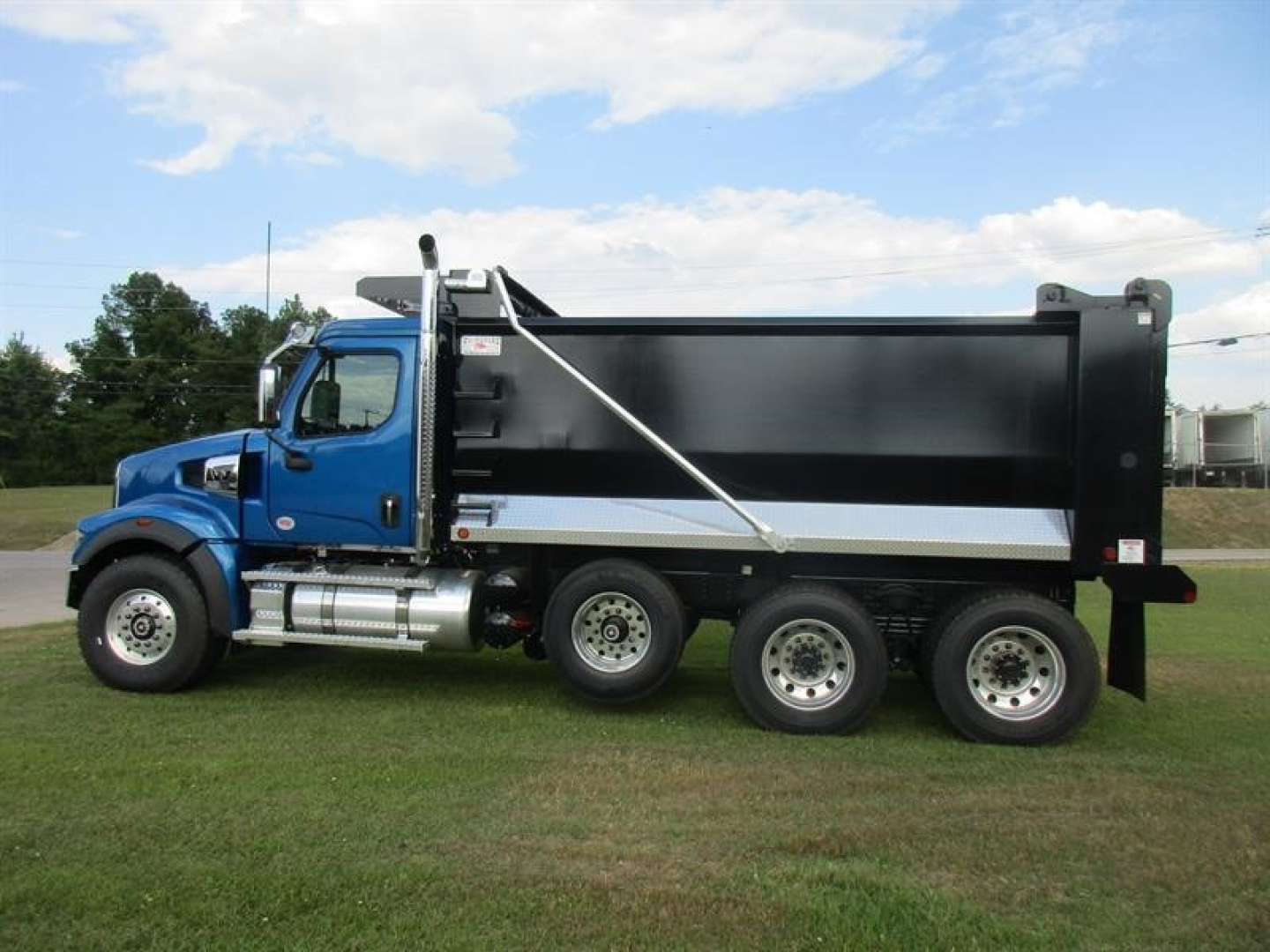 Blue Western Star 49X dump truck with black dump body and silver accents, side view on grass.