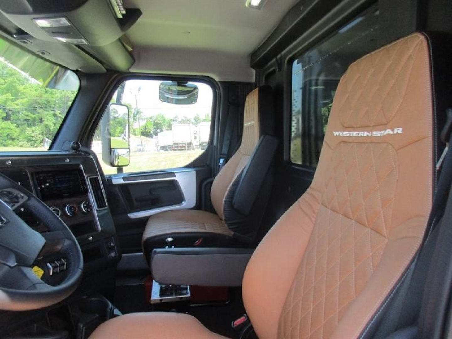 Interior of a new Western Star 49X dump truck cab showing tan diamond-stitched seats with Western Star branding, steering wheel, and driver's area.