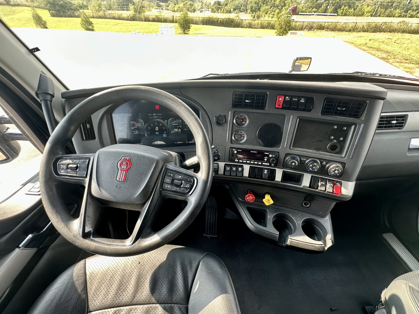Truck cockpit with Kenworth steering wheel and dashboard showing gauges and controls.