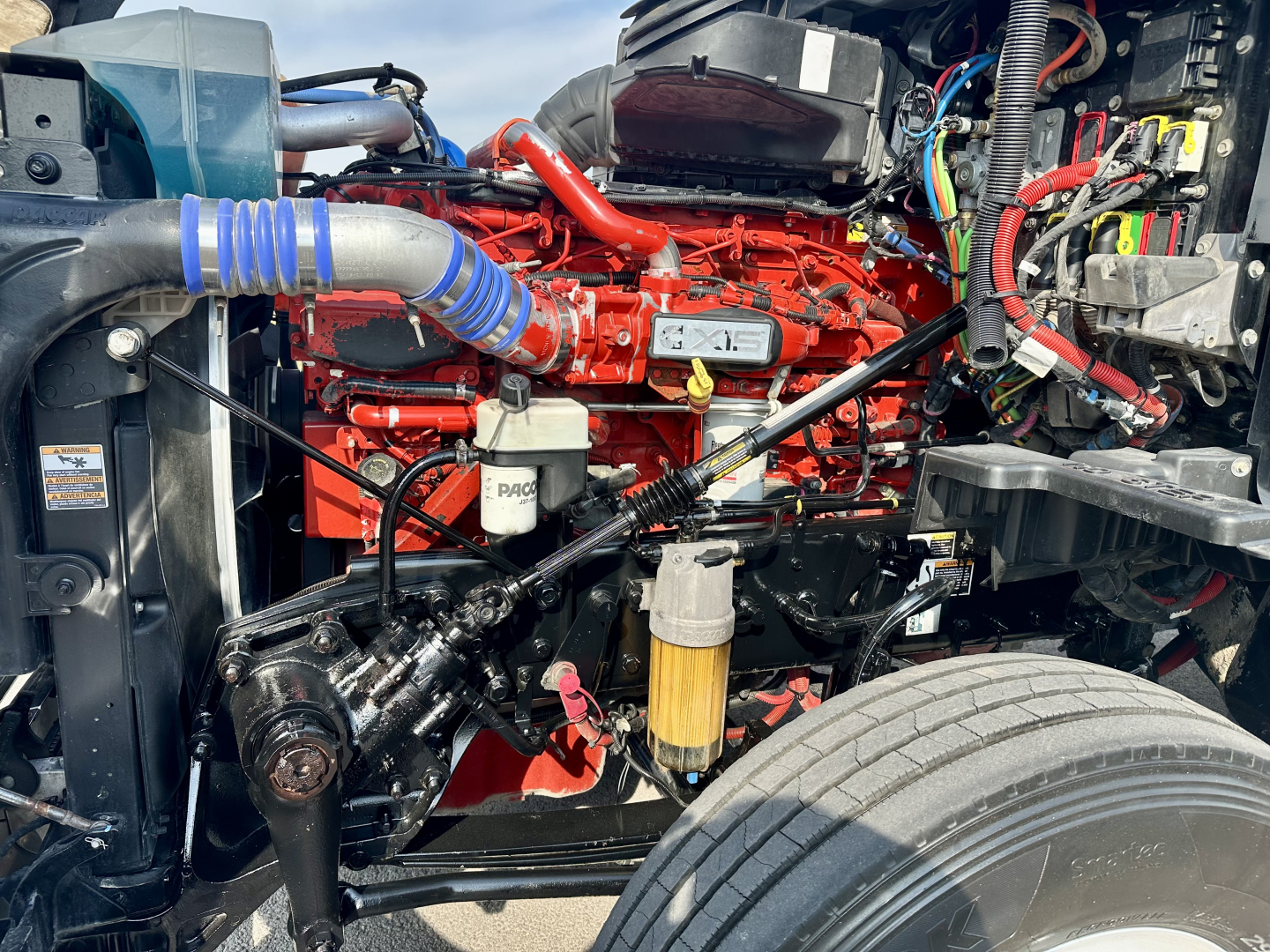 Kenworth T680 engine bay showing red diesel engine, hoses, filtration system, and surrounding wiring.