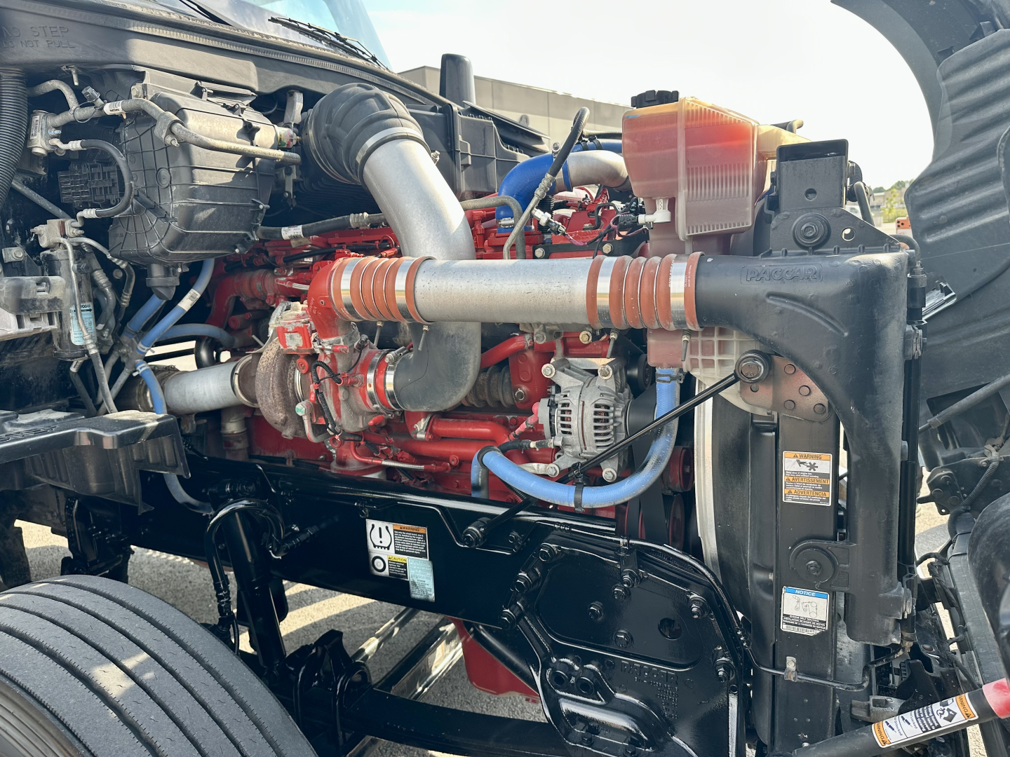 Kenworth T680 engine bay with red engine, hoses, and coolant reservoir visible; label badges and components in view.