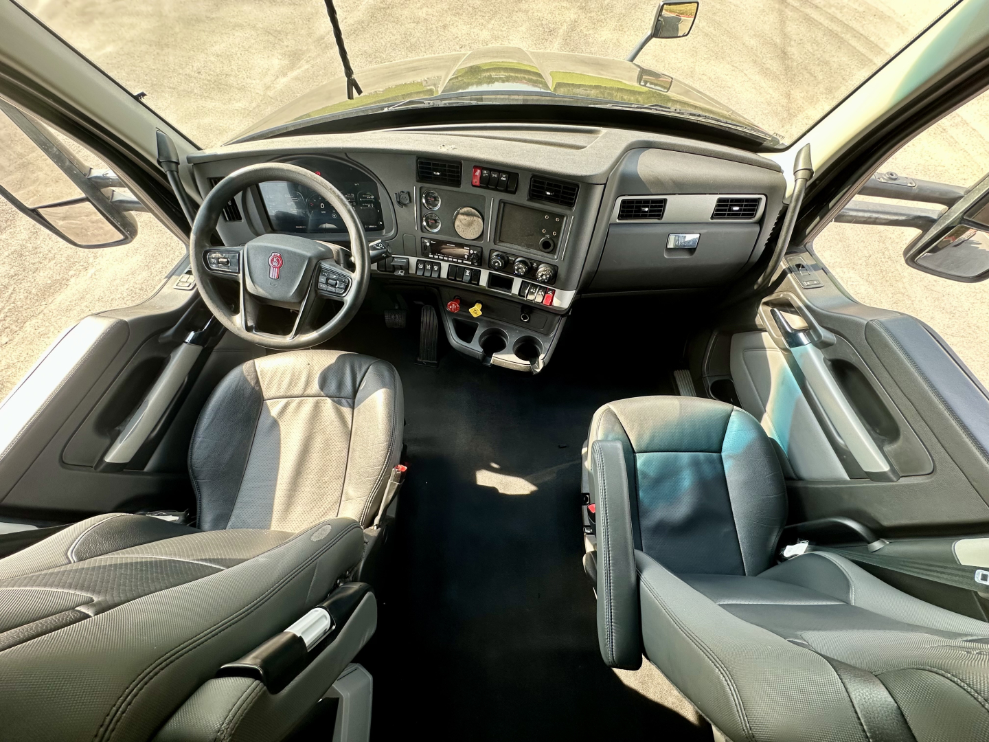 Kenworth T680 interior cab view showing steering wheel, dashboard with gauges, center console, and two seating positions.