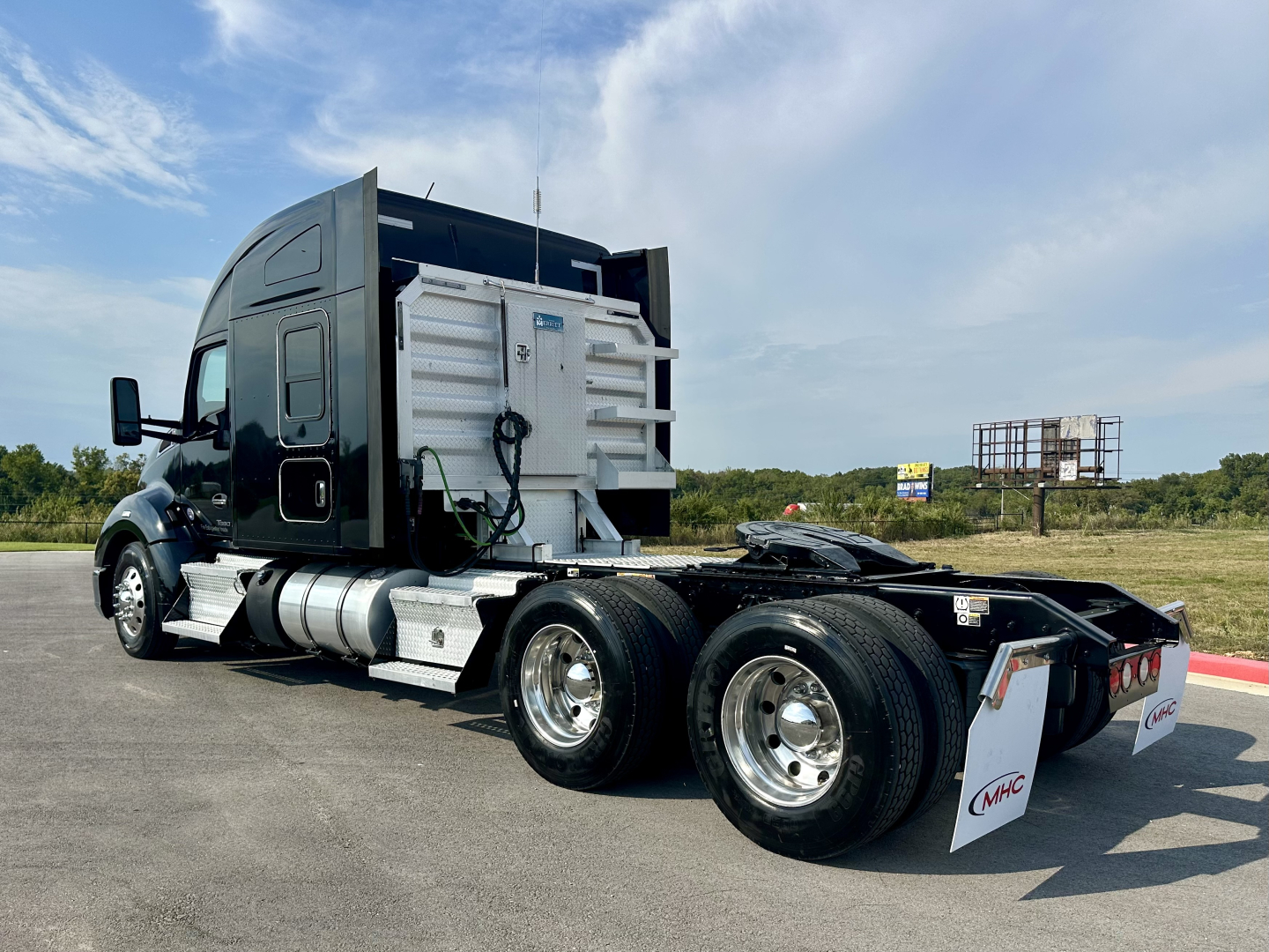 Kenworth T680 tractor truck rear view showing dual rear axles and fuel tanks, black cab, aluminum wheels, undercarriage components visible.
