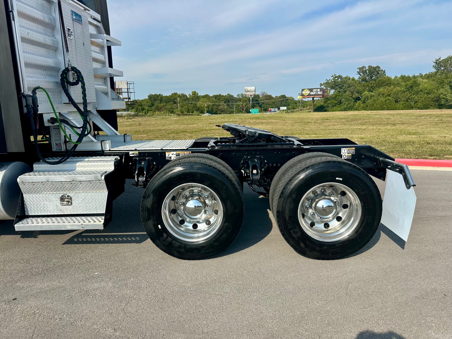 Kenworth T680 tractor rear dual rear wheels and fifth wheel assembly visible in side view. Chrome wheels, black chassis, aluminum tool boxes, white mud flaps, no cab in frame.