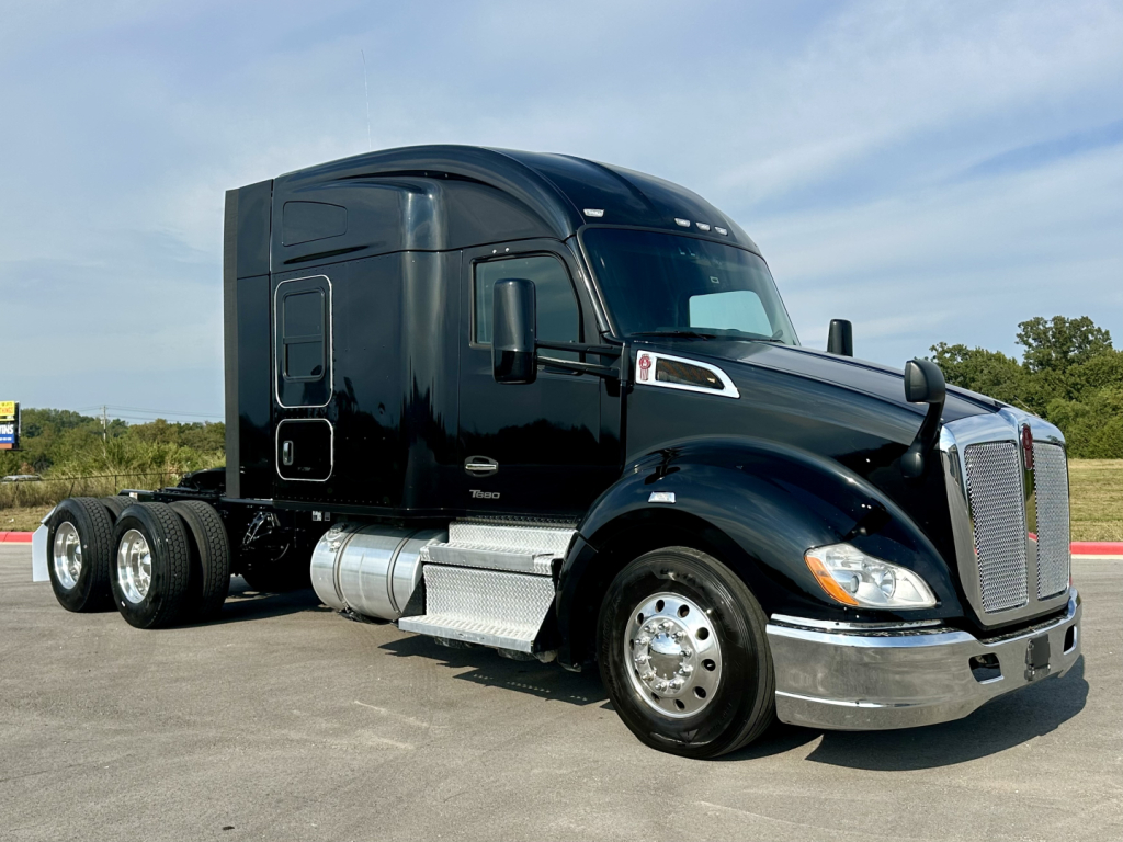 Kenworth T680 tractor in black paint, side view showing sleeper cab, front chrome grille, dual rear axles, fuel tanks, and highway environment.