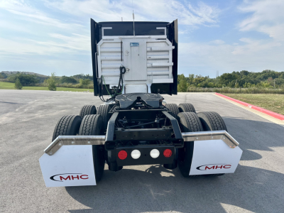 Kenworth T680 rear view showing sixth-wheel assembly and MHC white mud flaps with logos, truck chassis, and rear lights.