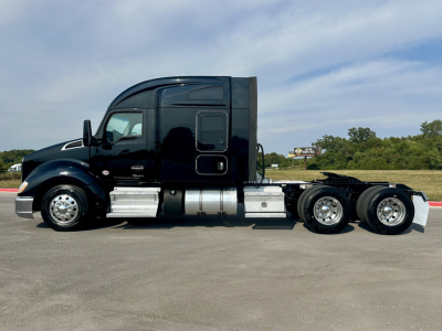 Kenworth T680 tractor side view showing glossy black cab, chrome fuel tanks, and triple rear axles. No visible text readable on components.