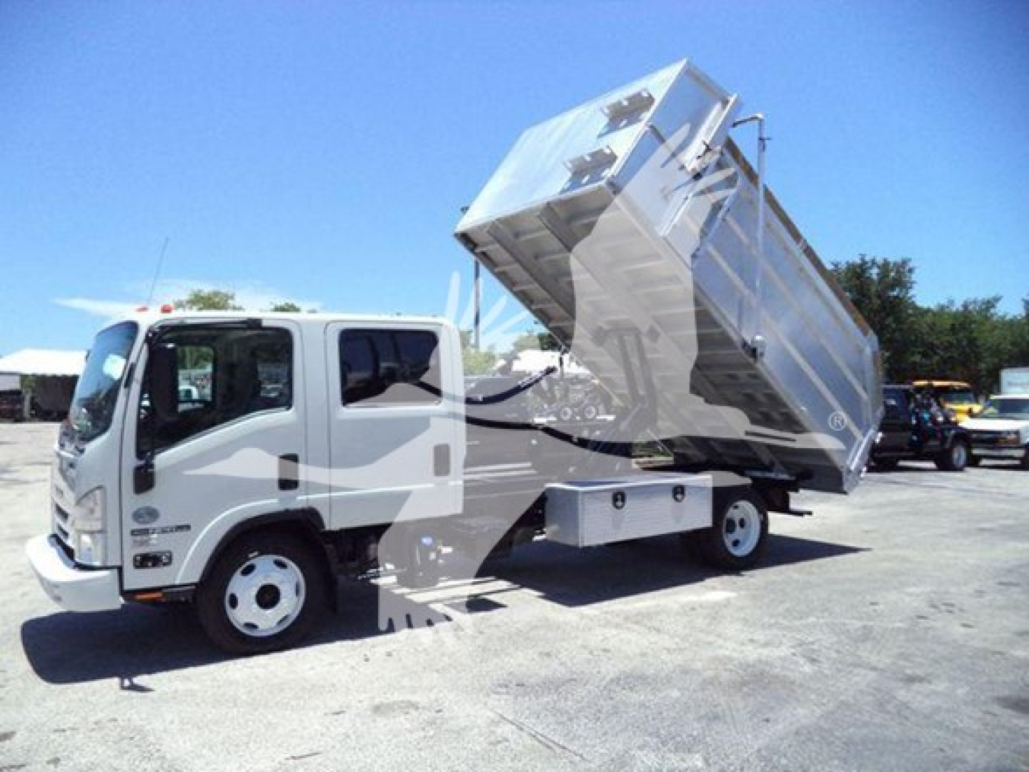 Isuzu NPR HD dump truck with raised metal dump bed in a lot, side view showing cab and front wheels.