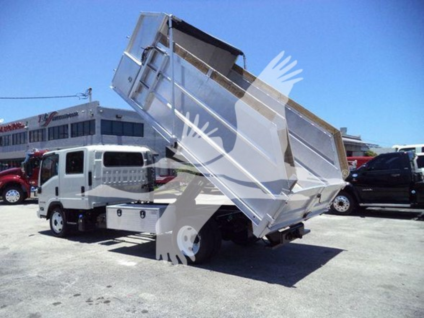 Isuzu NPR-HD dump truck with hydraulic dump bed raised in a parking lot, rear view showing metal dump body and truck cab.