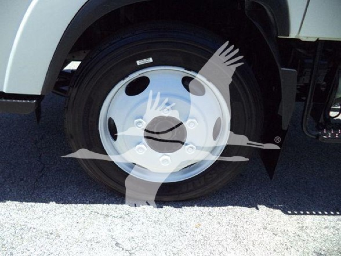 Isuzu NPR HD truck front wheel showing wheel cover and tire, part of a dump truck configuration.