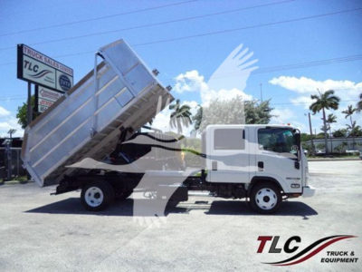 Isuzu NPR HD dump truck in side view with dump bed raised, white cab and silver dumping bed, dealership lot background