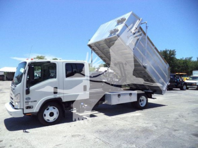 Isuzu NPR HD dump truck with raised metal dump bed in a lot, side view showing cab and front wheels.