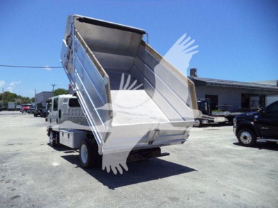 Isuzu NPR HD dump truck with raised bed in a truck lot, side view showing empty tipping container and rear hydraulic mechanism.