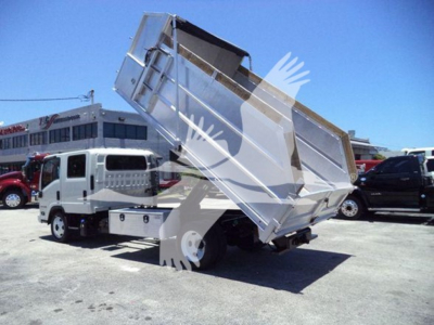 Isuzu NPR-HD dump truck with hydraulic dump bed raised in a parking lot, rear view showing metal dump body and truck cab.