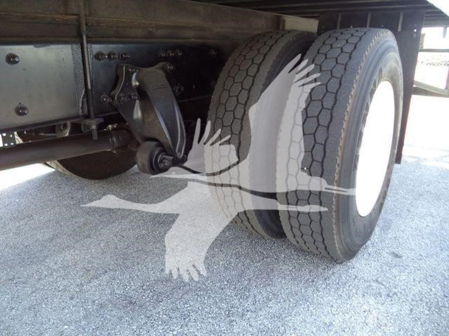 Truck rear axle and dual tires of a 2016 Freightliner M2 106; undercarriage shows suspension hanger and leaf spring; white wheel rims visible.