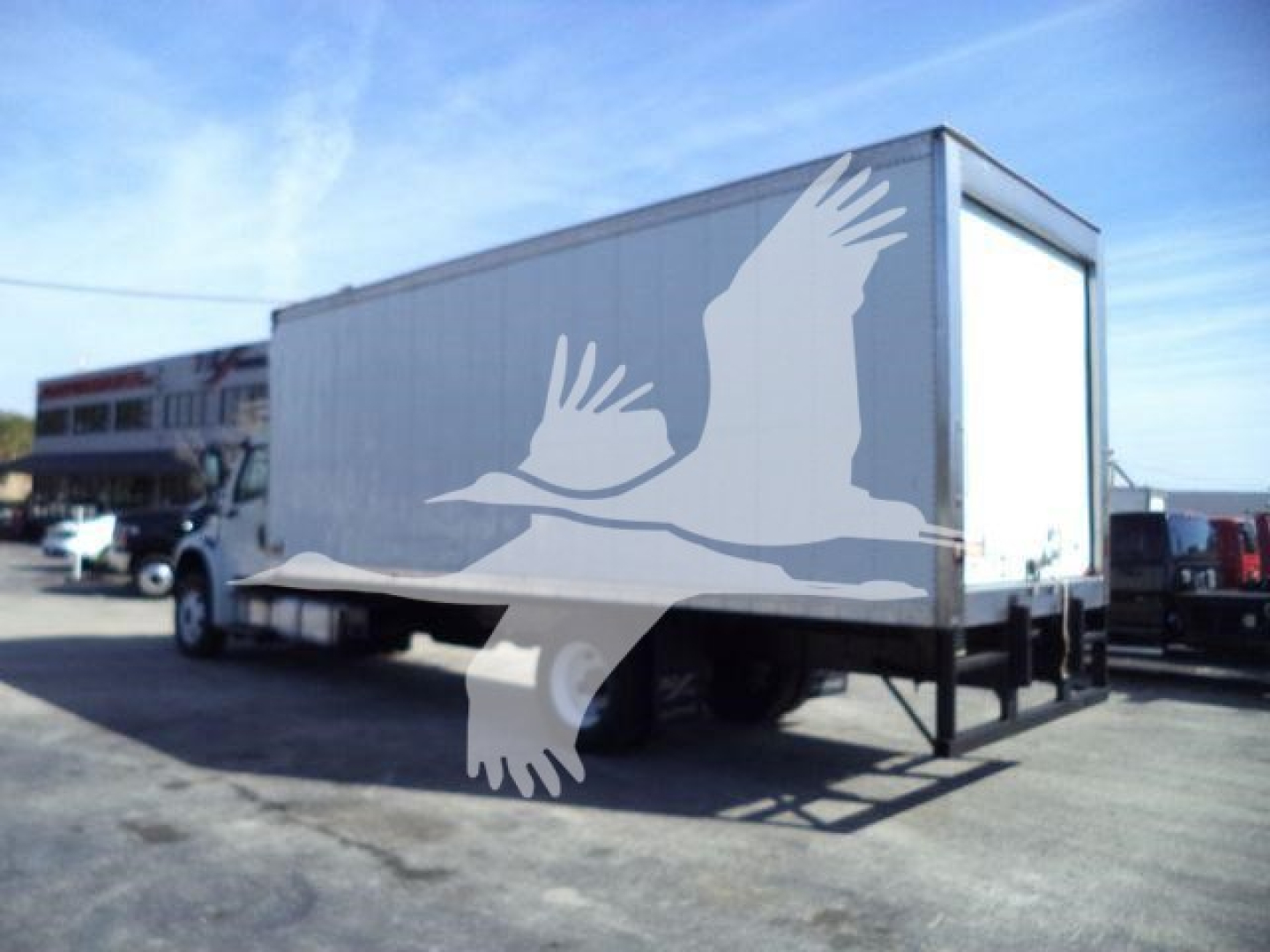 Refrigerated box truck seen from side, Freightliner M2 106 with white cargo box mounted on chassis; watermark of a bird overlay in the foreground.