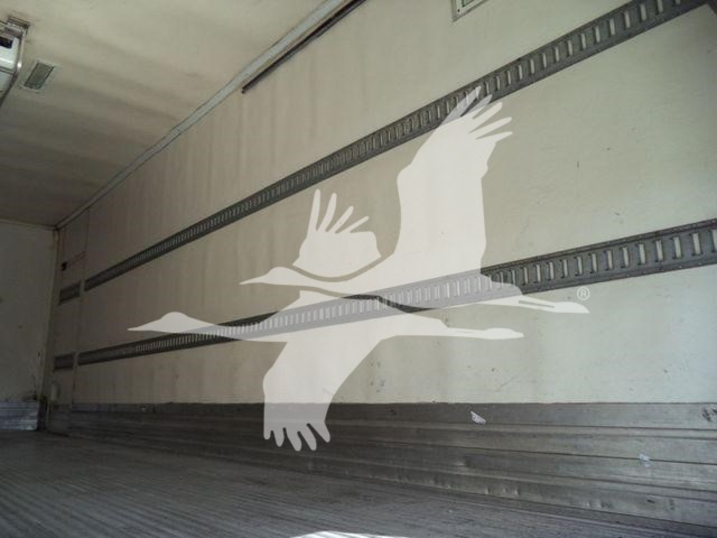 Truck trailer interior with metal side rails and a large white bird stencil on the wall.