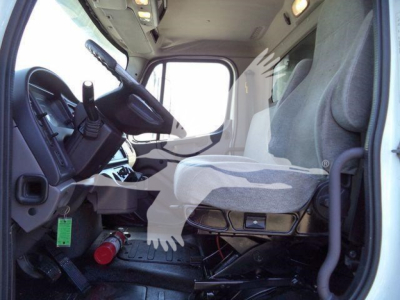 Cab interior of a Freightliner M2 106 truck showing driver seat, steering wheel, and dashboard with a gear shifter and pedals.