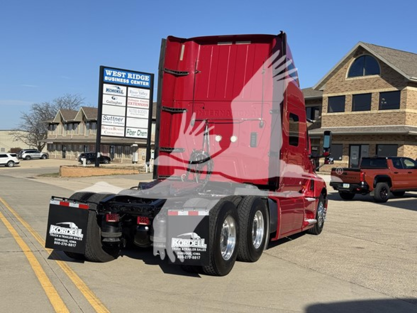Truck rear view showing red cab and dual rear axles with mud flaps and license plate area.