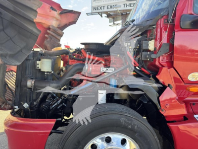 Engine bay of a red 2018 International LT truck showing components and hoses around the engine, with a visible front wheel and air intake area.